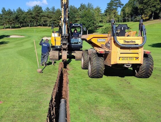 A low-pressure tracked excavator laying a deep drain on a fairway