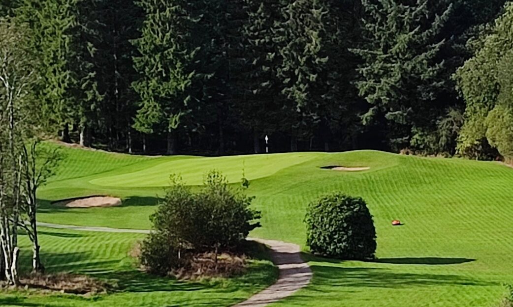 A robotic mower working on a golf course fairway, with green surrounds and mature trees in the background