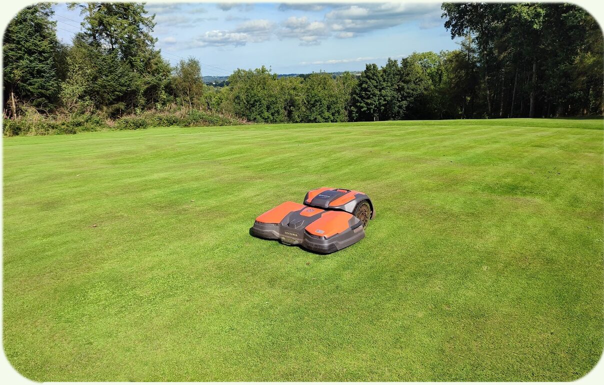 A robotic mower working on an open fairway with rolling countryside in the background
