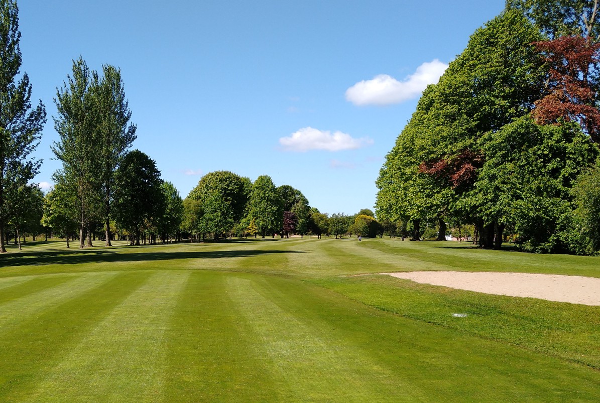 A firm fairway framed by trees and a bunker under a clear blue sky, showing a course in good heart throughout the year