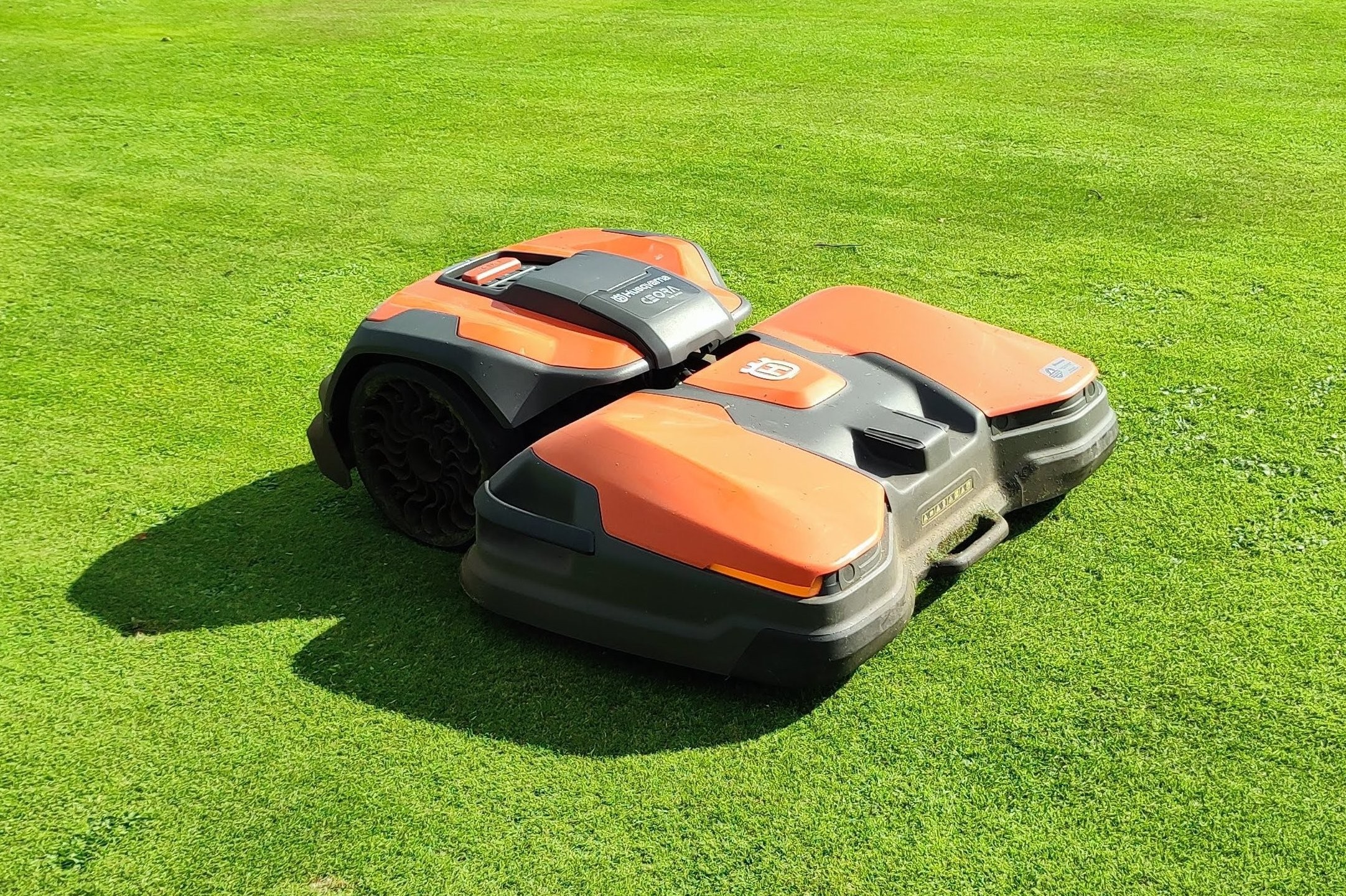 An orange Husqvarna robotic mower parked on a sunlit fairway